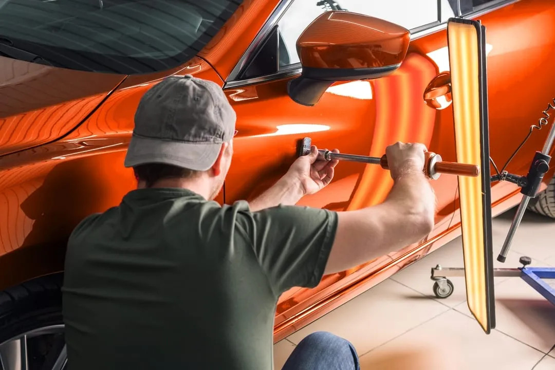 Close-up of a technician using specialized tools to carefully remove a dent from a car panel.