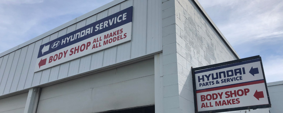 Exterior of a car body shop with signs, indicating a vehicle repair service location for insurance claims.