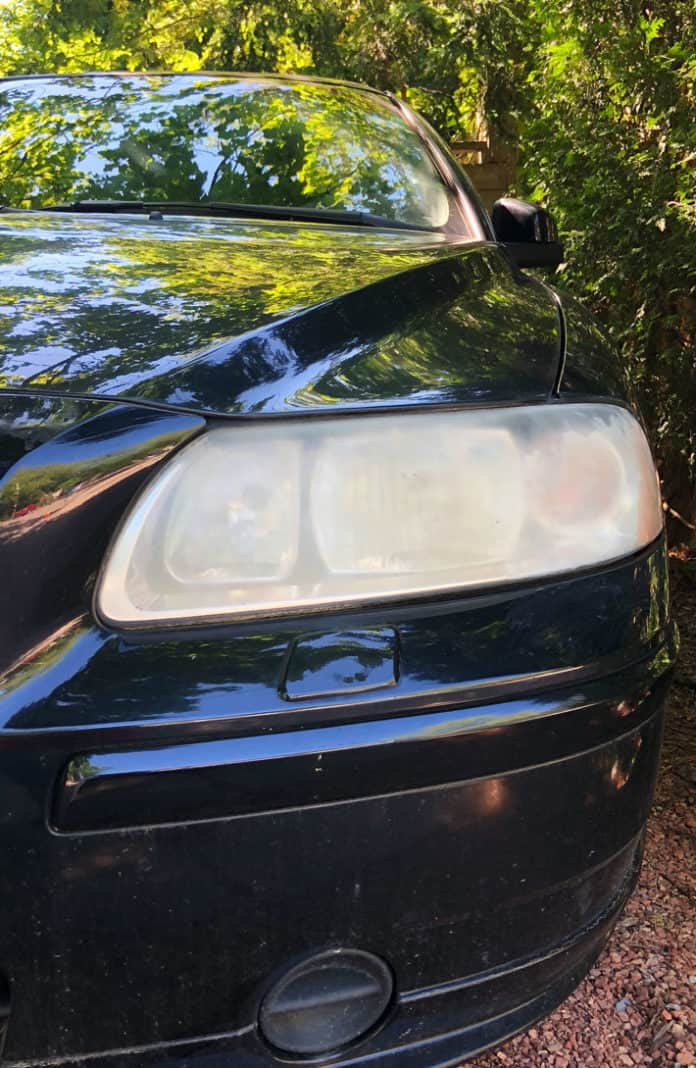 Close up of a severely cloudy car headlight showing the opaque plastic lens.