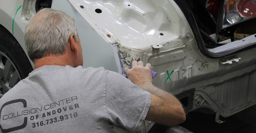 Skilled auto body repair technicians repairing a dented car door panel in a professional shop.