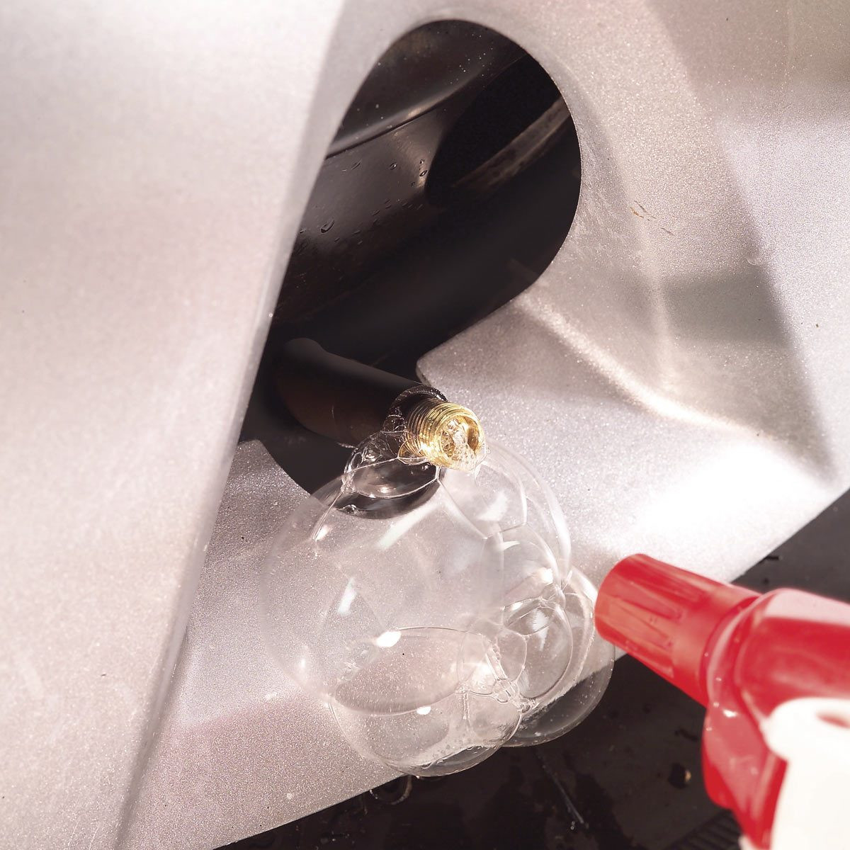 Using soapy water to check for leaks around a car tire valve stem, indicated by bubbles forming.