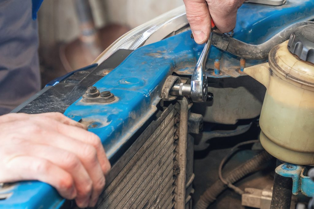 A mechanic using a wrench to disconnect a component during a car radiator repair, highlighting the labor involved in professional fixes.