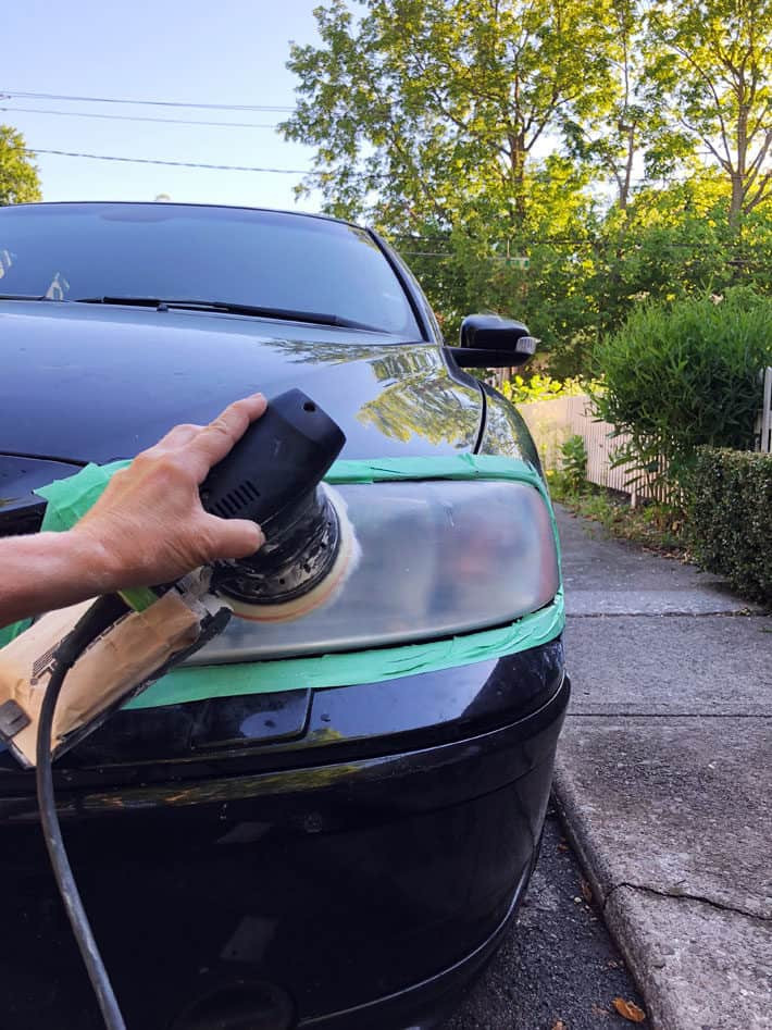 Polishing a headlight using a hand sander with a wool buffing pad.