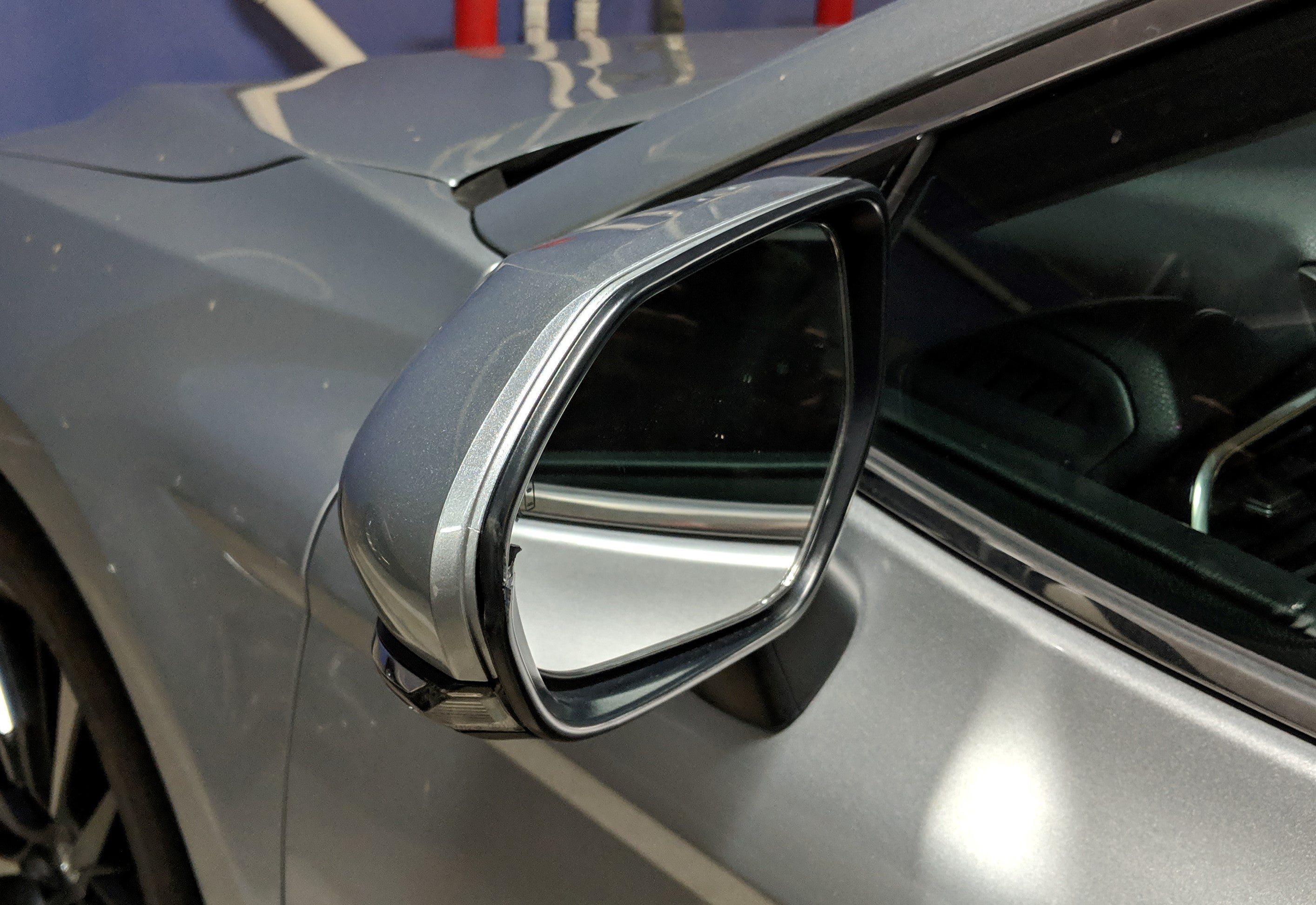 Damaged car side mirror on a Toyota vehicle, showing a cracked black frame but an intact mirror and silver shell, illustrating a common parking accident