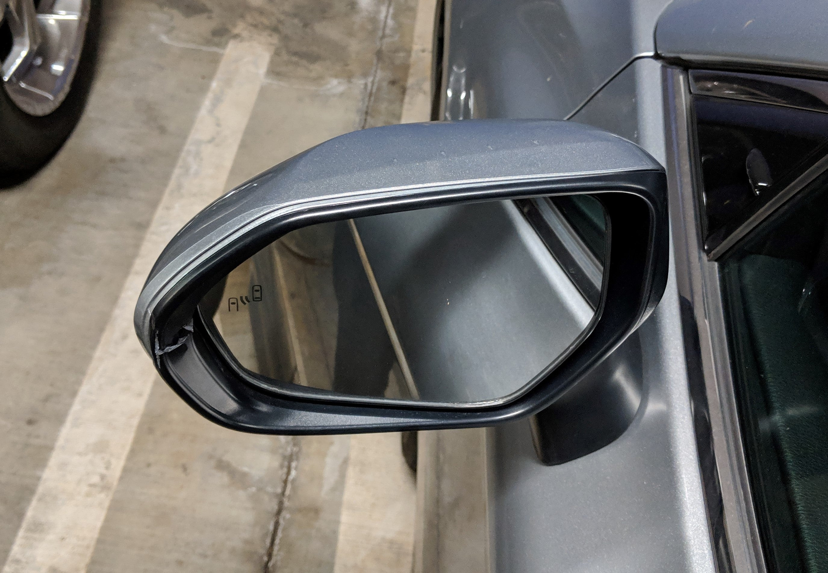 Close-up of a cracked car side mirror frame on a Toyota, highlighting the damage to the black plastic housing after hitting a column while parking