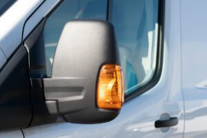 Close-up of a truck side mirror with illuminated turn signal, indicating a lane change.