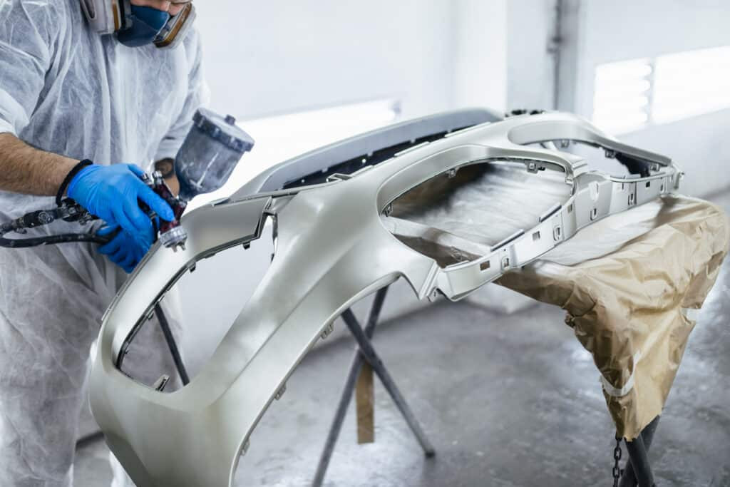 Technician carefully repairing a car bumper in a workshop.