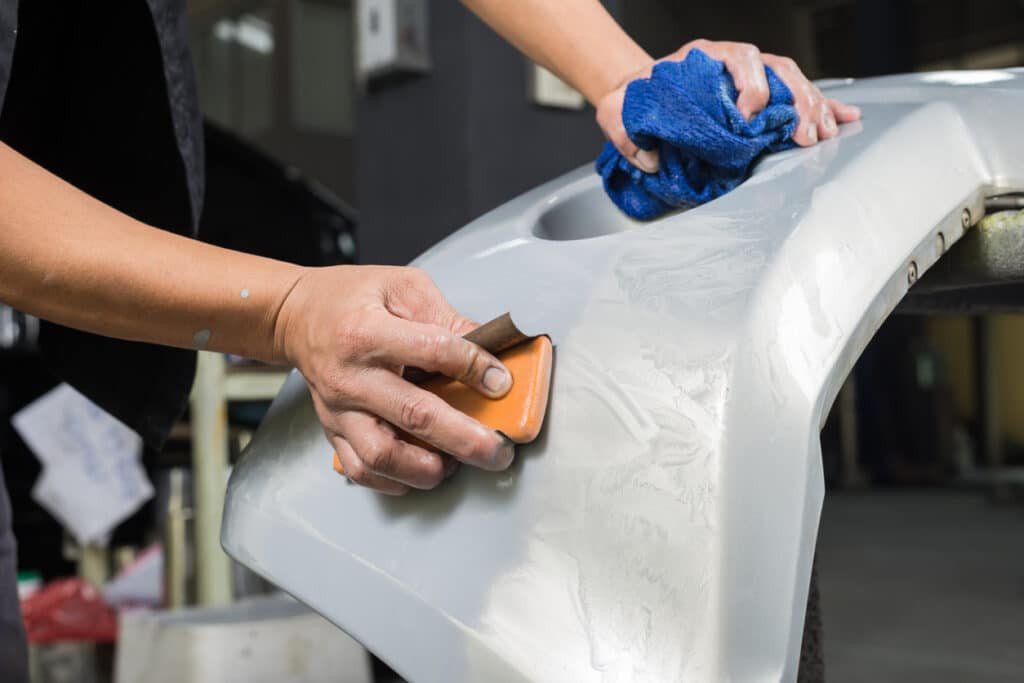 Hands meticulously cleaning a car bumper, preparing it for repair.