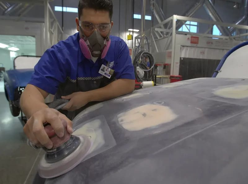 Technician grinding down a plastic car part for repair